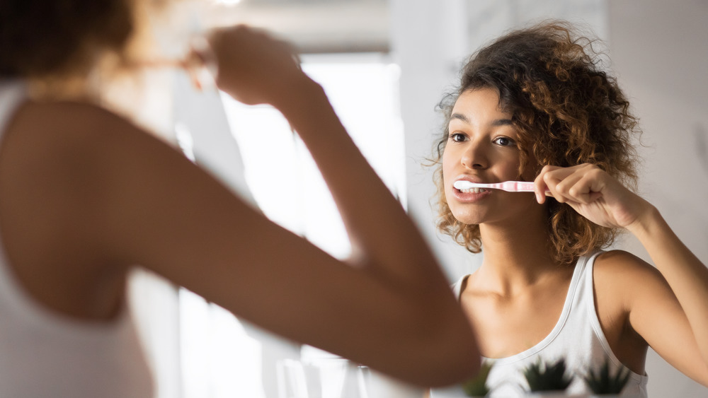 Woman brushing teeth in mirror