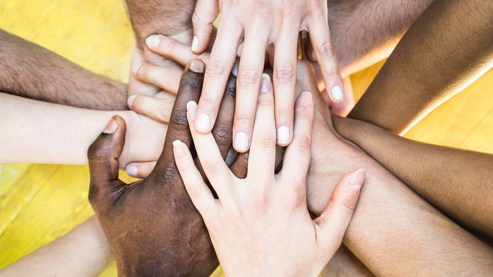 Hands of people of different races reaching into the middle together