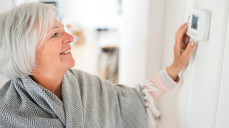 Older woman wrapped in blanket setting thermostat