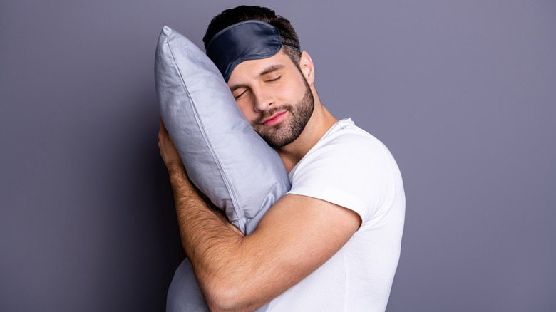 Closeup portrait of bearded guy holding pillow in front of purple background