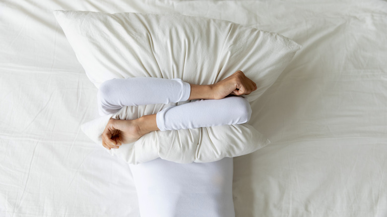 Top view of woman in bed holding pillow over her facee