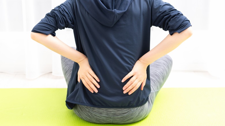 Close up on backside of person sitting down on a green mat holding their back hips in pain
