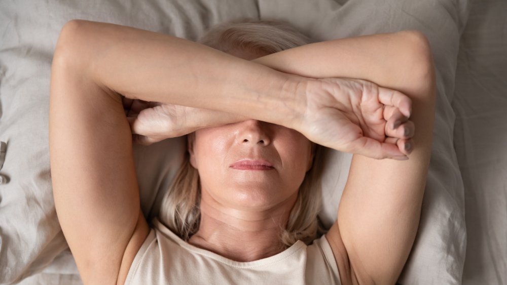 Sleepless woman close up, lying in bed, covering eyes with hands feeling headache or migraine