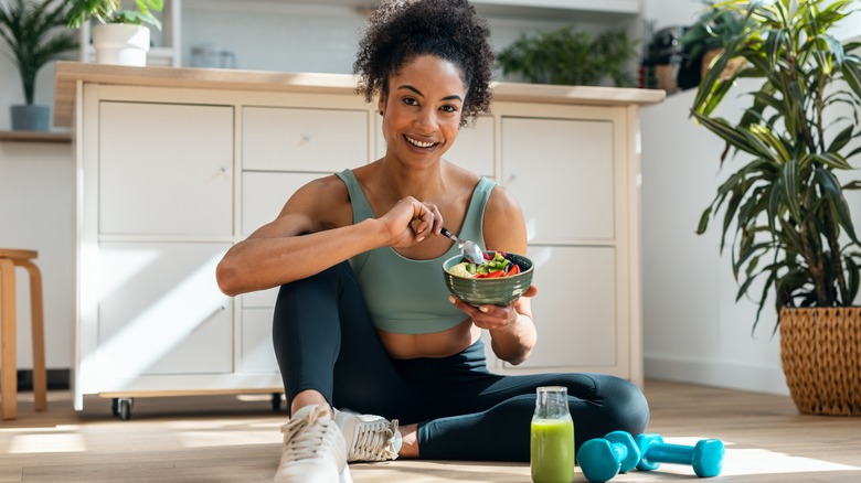 fit woman sitting on kitchen floor eating bowl of fruit