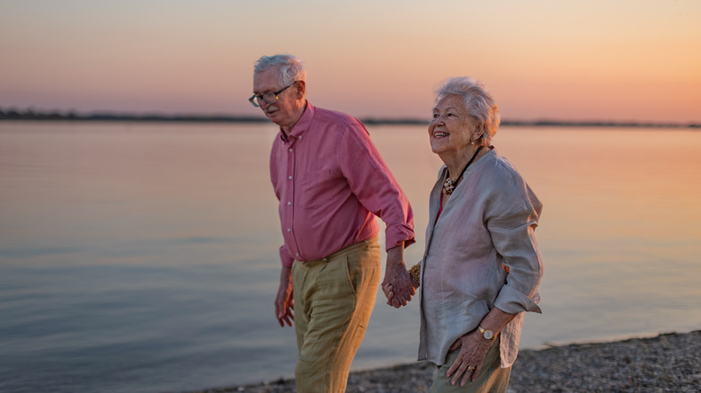 older adult couple walking on a beach at sunset