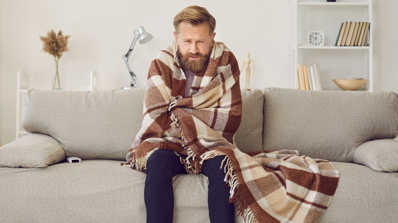 Man wrapped in blanket sitting on couch shivering