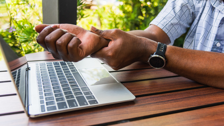 Close up of a man's hands over a laptop as he rubs his wrist