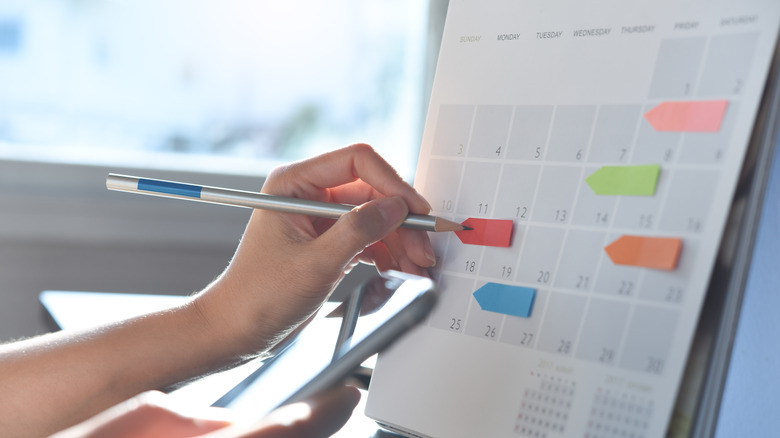 ﻿﻿Event planner timetable agenda plan on schedule event. Woman checking planner on mobile phone, taking note on calendar desk on office table. 