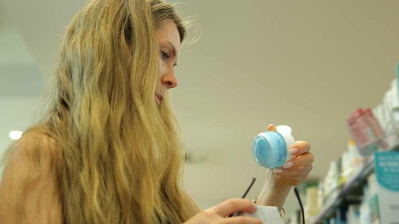 woman examining moisturizer jar ingredients in store