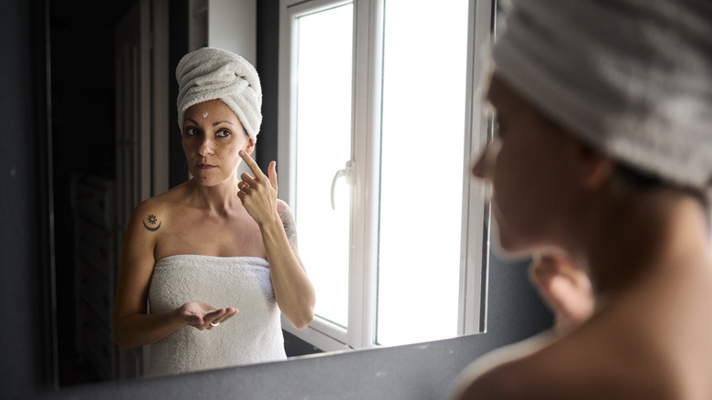 woman putting skin cream on face in mirror