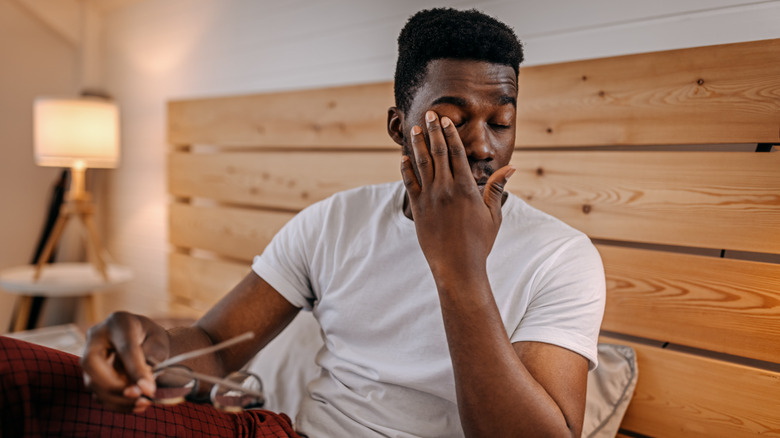 man rubbing his eyes while in bed