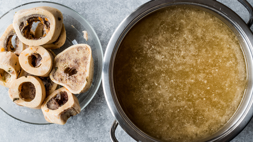 A metal pot of broth next to a bowl of bones