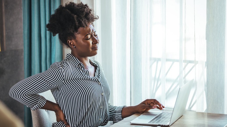 Woman at desk holding lower back