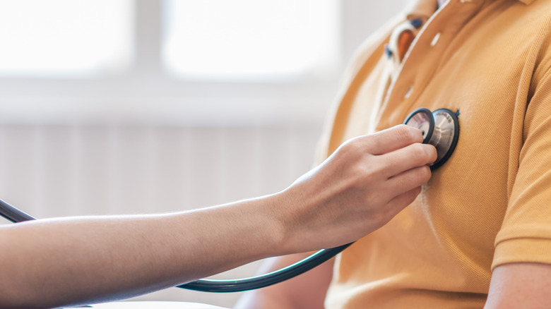 A medical professional's hand using a stethoscope to measure a man's heart