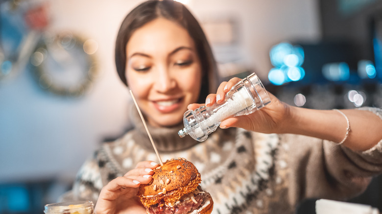 woman adding salt to a hamburger