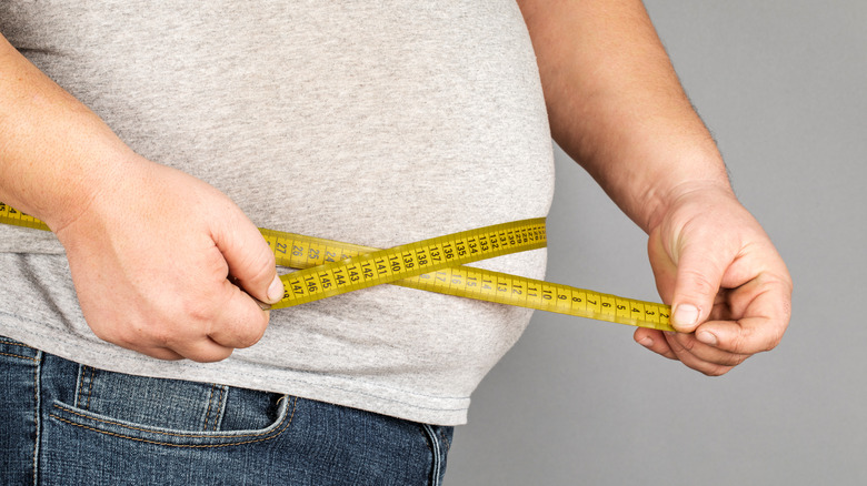 obese man measuring waistline 