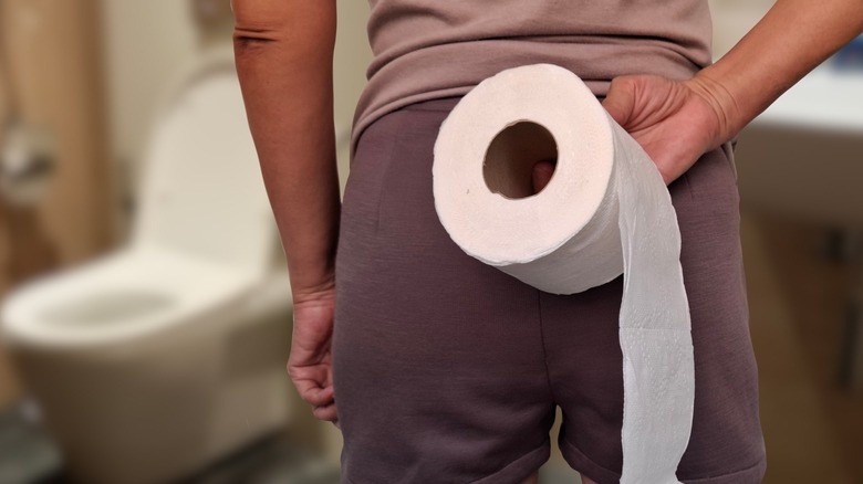 Person in bathroom holding roll of toilet paper
