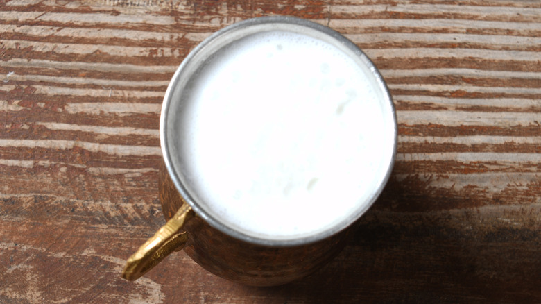 Overhead shot of buttermilk in a copper cup on a piece of wood