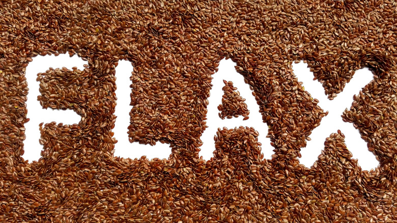 The word "flax" written in the spaces in a pile of flaxseeds