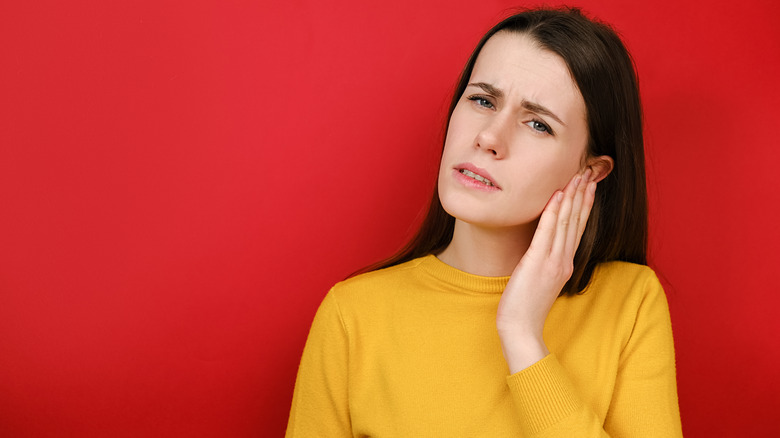 Woman against a red background, holding her ear in discomfort