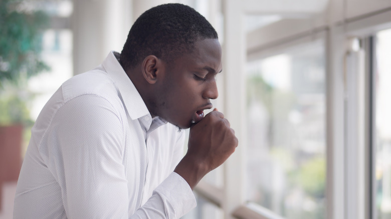 Man coughing into his hand next to windows