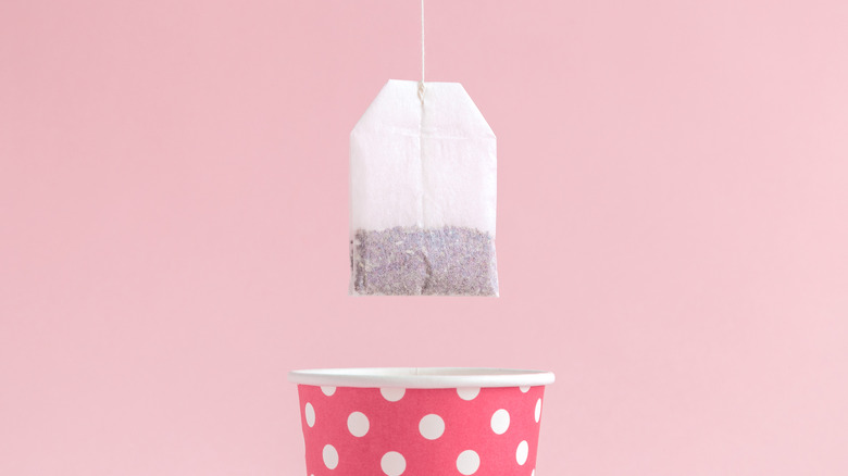 A tea bag being dangled above a pink cup with white spots against a pink background 