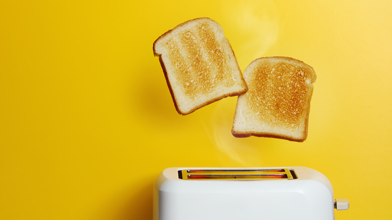 Two pieces of toast popping out of a white toaster against a yellow background