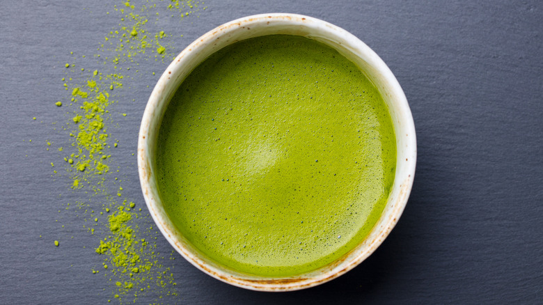 Overhead shot of a cup of green tea with green tea powder sprinkled next to the cup