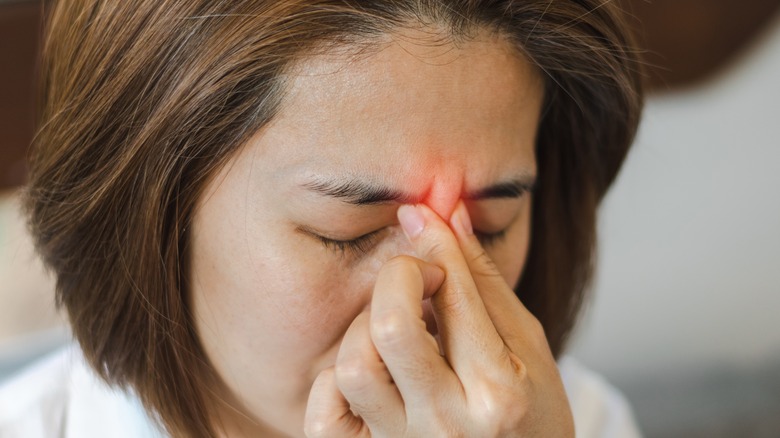 Woman winces and presses fingers to the bridge of her nose in pain