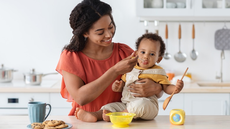 Mother spoon feeding infant in kitchen