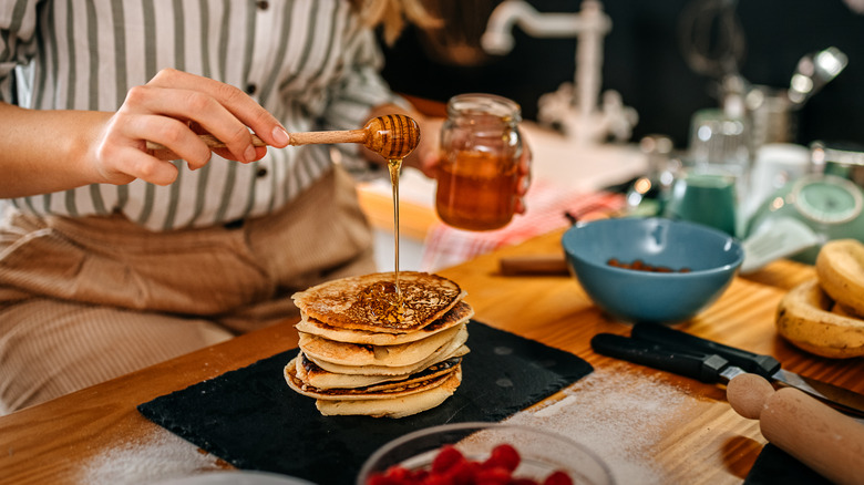 woman adding honey to pancakes