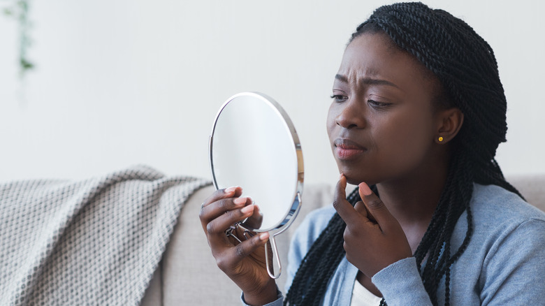 Woman studying her face in a hand mirror