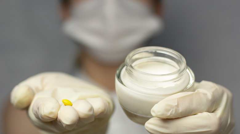 A person with gloved hands holding pills and cream