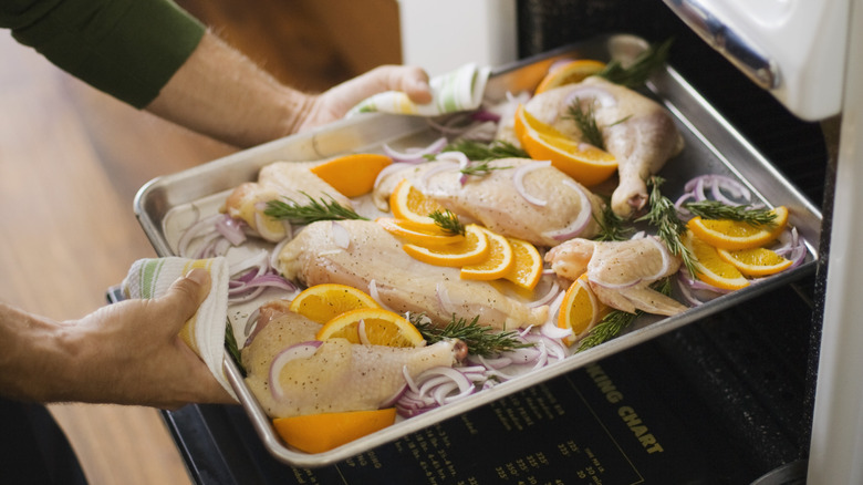 Hands placing tray of chicken in oven