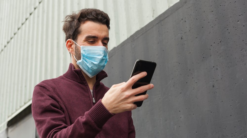 Man wearing face mask checks phone outdoors