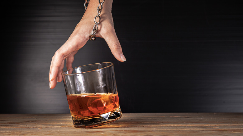 hand bound by a chain reaching for glass of alcohol