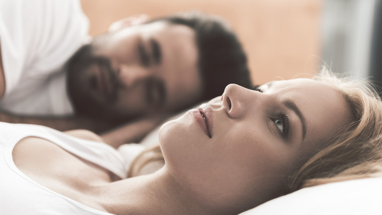 An anxious woman laying in bed with her partner