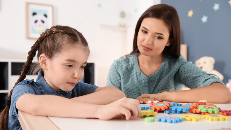young girl sitting with therapist completing puzzle