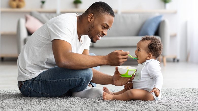 father sitting on floor feeding baby