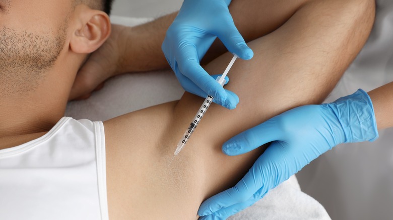 Cosmetologist injecting man's armpit with Botox