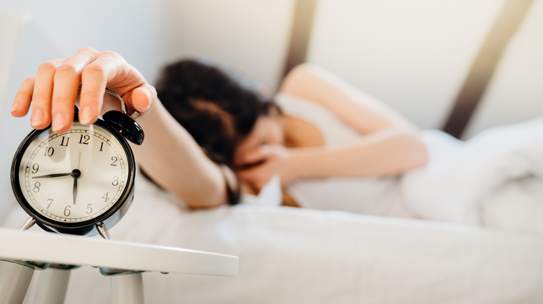 Woman turning off alarm clock looking sleep-deprived