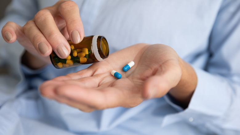 Woman holding two pills in hand while pouring capsules from medication bottle