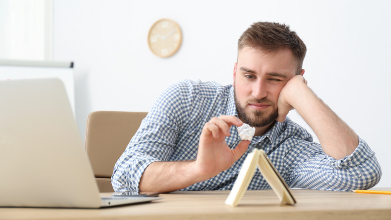 procrastinating man playing with ball of paper