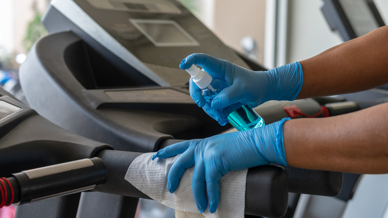 Gloved hands wiping down gym equipment 