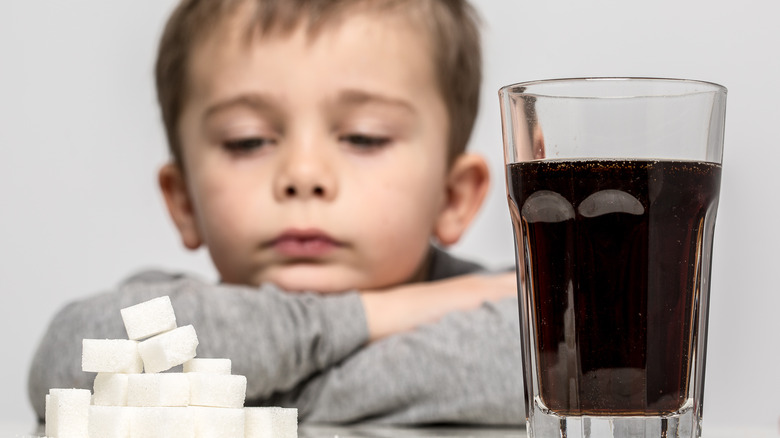 Child staring at sugar cube pile and soda glass on table