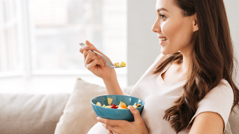 Woman sits on couch with bowl of healthy food