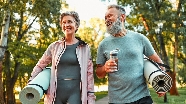 An older man and woman carrying exercise mats while walking outdoors