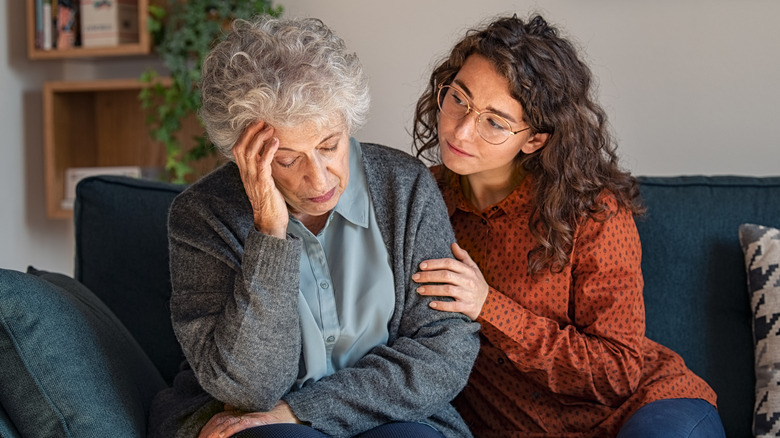 Young girl comforts a grieving elderly woman on couch