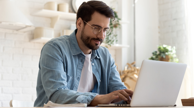 Focused young man wearing glasses using laptop