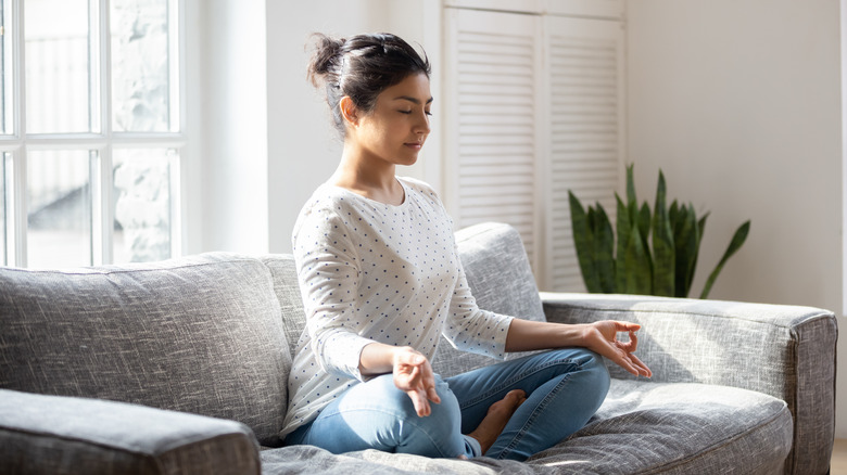 Woman sitting on couch in lotus pose meditating